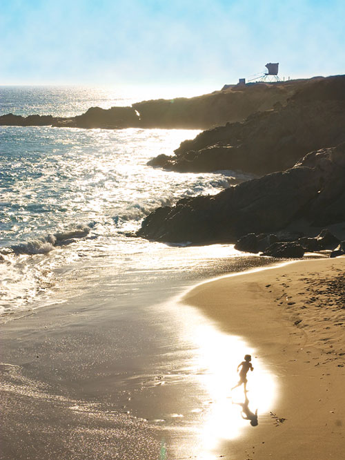 Silhouetted by the sun reflecting off the waves, a young boy runs on the sand of Leo Carillo State Beach.