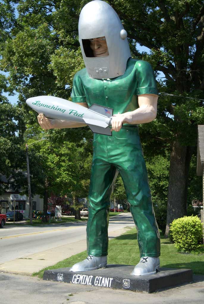 A statue of a green-suited spaceman holding a rocket.