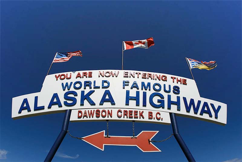 View of flag-bearing sign reading You Are Now Entering The World Famous Alaska Highway, Dawson Creek BC