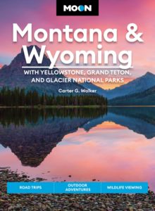 Book jacket of the Moon Montana and Wyoming travel guide featuring an image of mountains reflected in a lake during a pink sunset