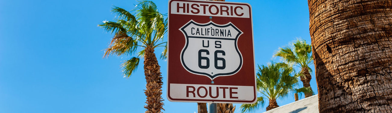 Looking up at a Historic Route 66 Sign in Needles California with palm trees in the background