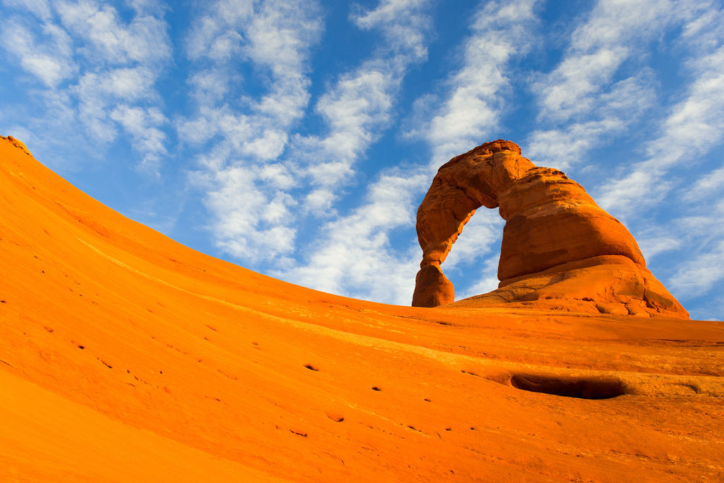 orange sand with a single sandstone arch under blue sky
