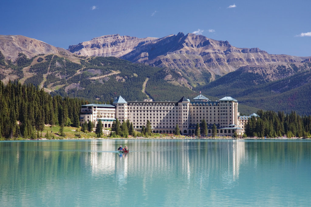 aquamarine lake with a hotel and mountains in the background