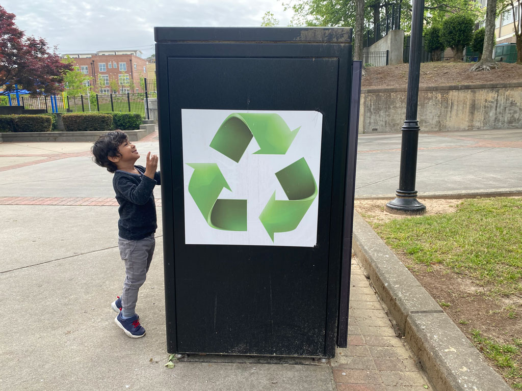 young boy next to a recycling bin